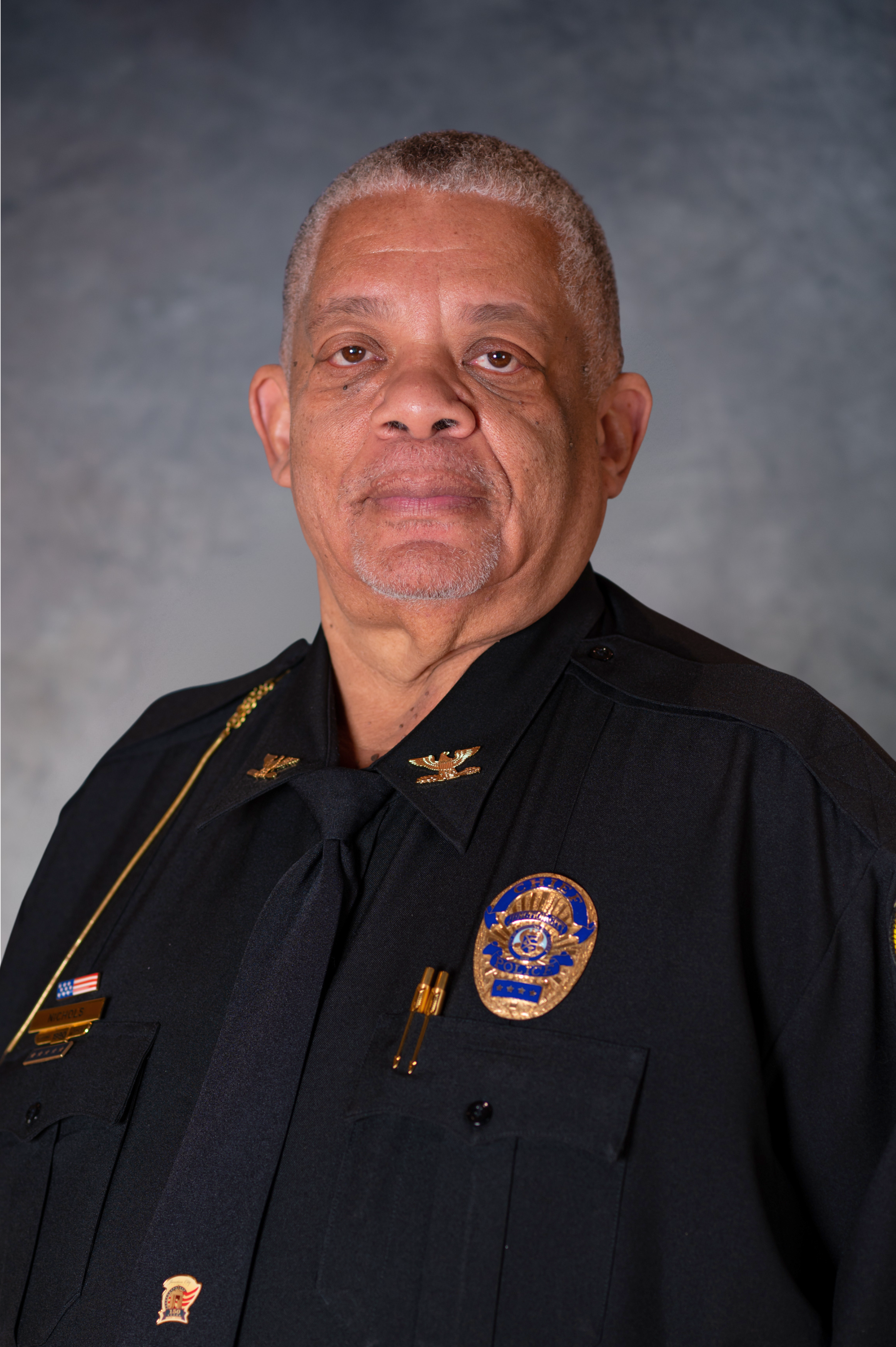 Older man with buzz cut looks directly at camera wearing police dress uniform