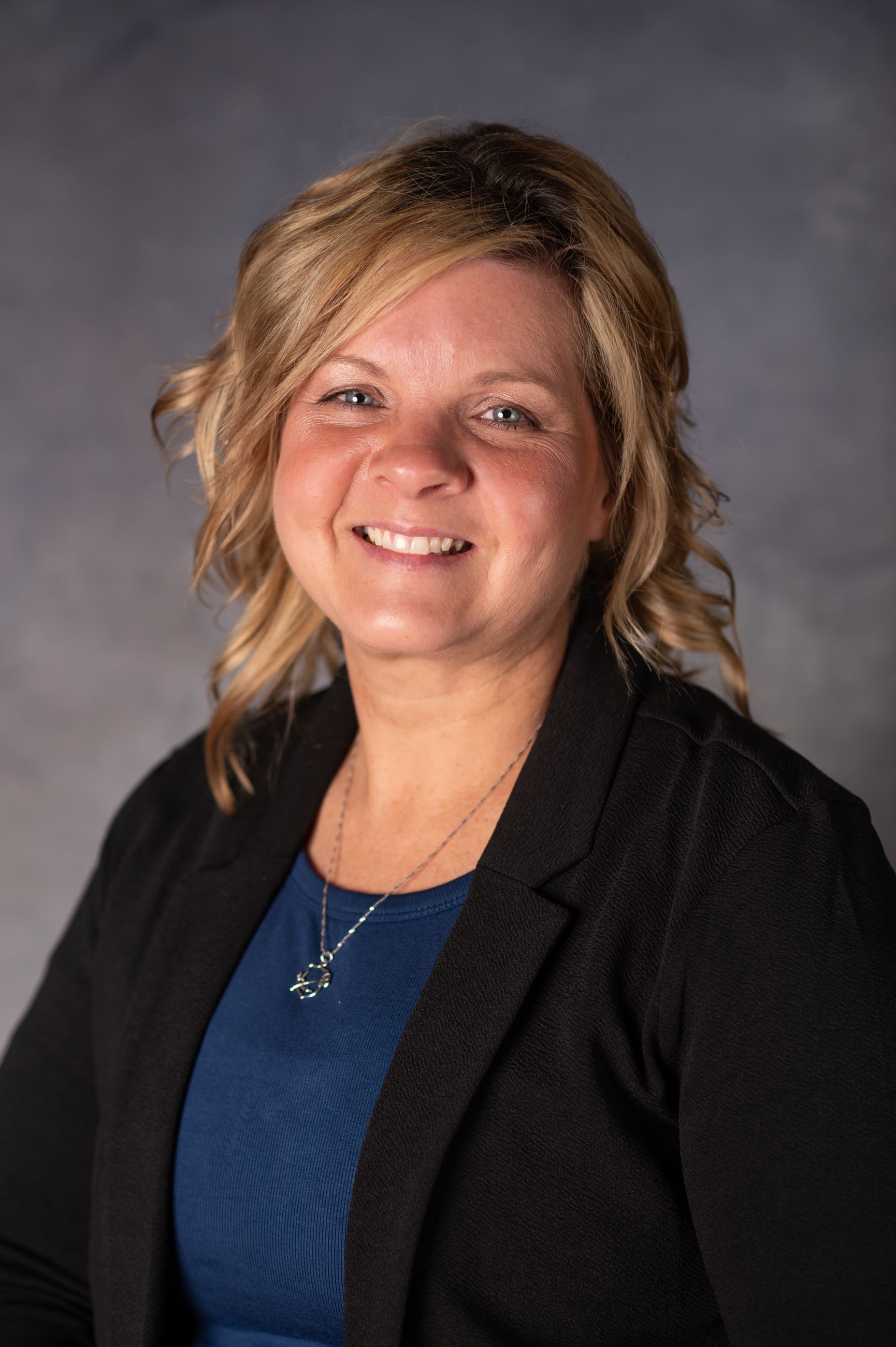 Blonde woman wearing blue blouse and black blazer smiling directly at camera