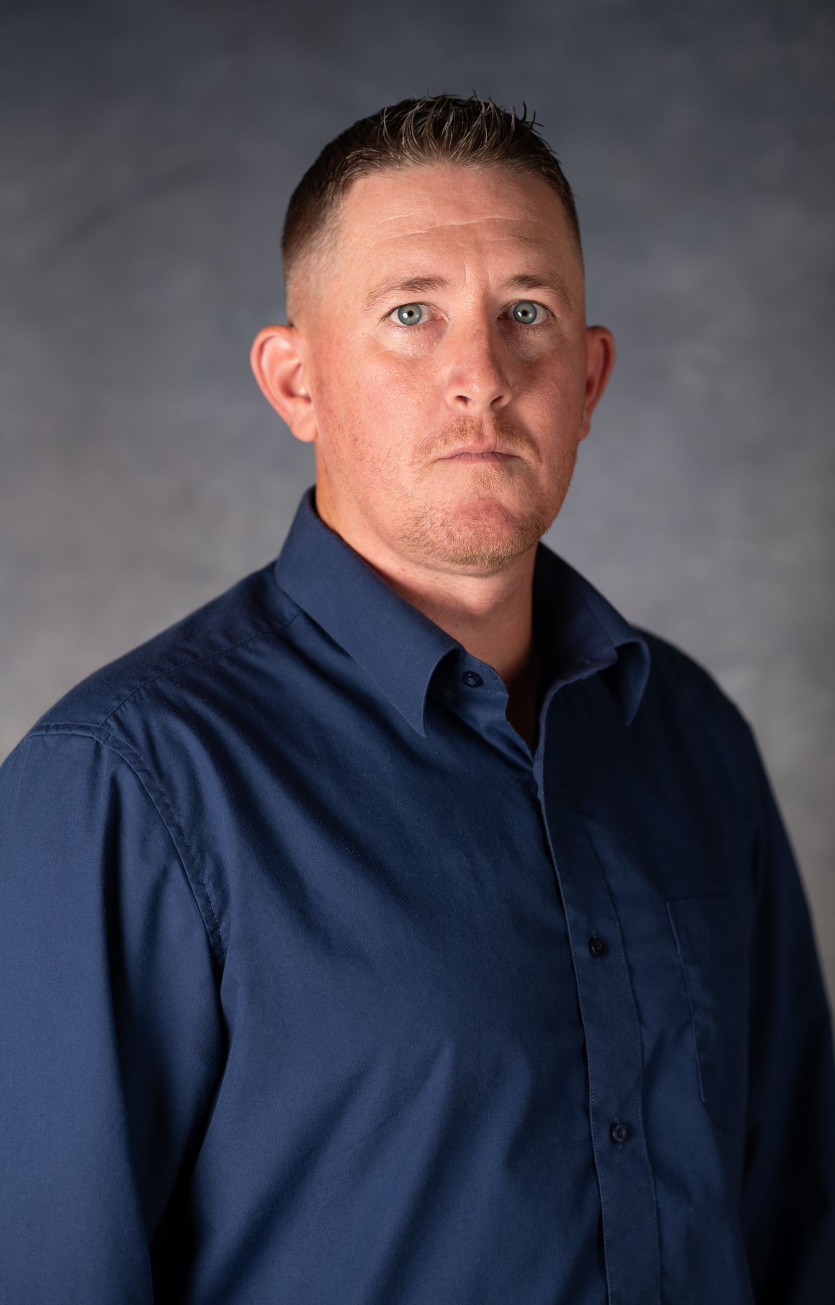 Man in blue collared shirt looking directly at camera.