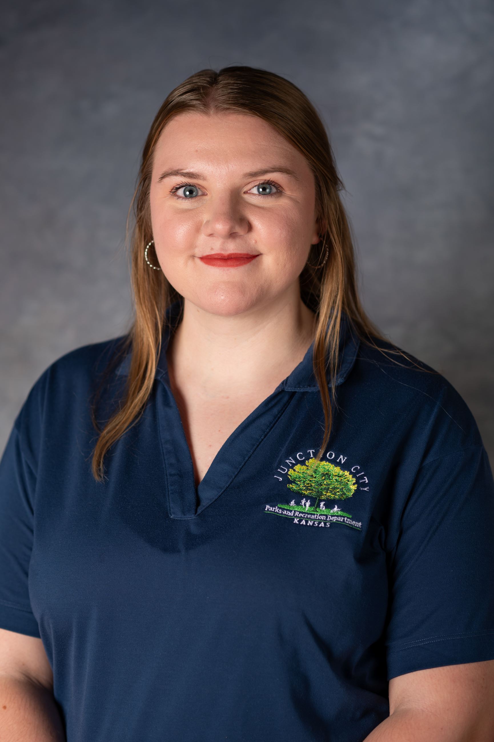 Young woman with light brown hair smiles at camera in blue button up.